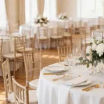 Eleganckie kompozycje kwiatowe z piwonii i róż na stołach weselnych w jasnej sali